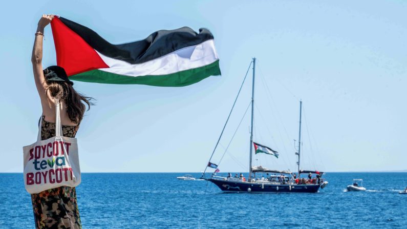Sur le quai de San Giovanni Li Cuti, une femme brandit le drapeau palestinien peu avant le départ du Madleen pour Gaza, le 1er juin 2025 à Catane, en Italie. (Fabrizio Villa/Getty Images)